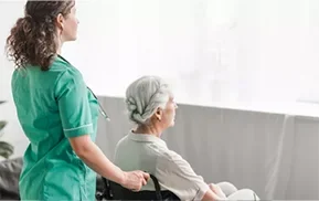 Zorgprofessional assisteert oudere vrouw in rolstoel bij het kijken naar buiten.